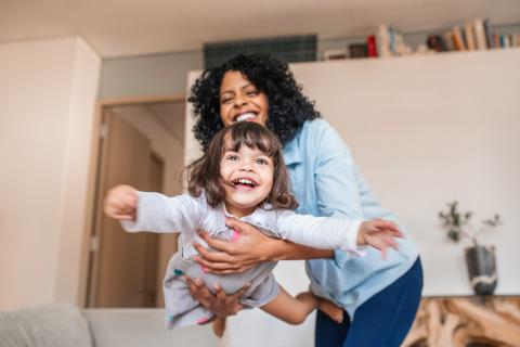 mum holds toddler by supporting her stomach. toddler has her arms out and is smiling