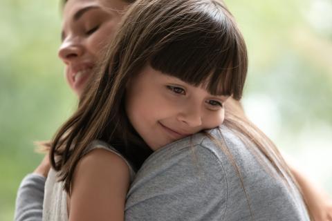 Smiling child puts her head on her mothers shoulder