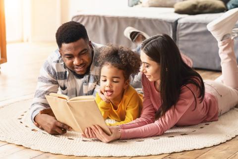 Mum, dad and daughter lying on the floor reading a book together