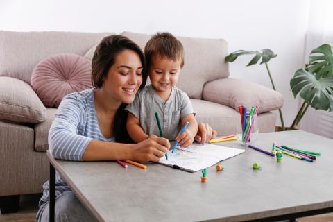 Mother and young boy sit on the floor at a table, drawing with coloured pencils and paper