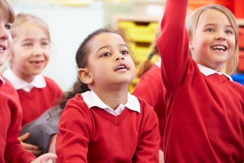 Children sat on the floor wearing red uniform jumpers and white shirts underneath
