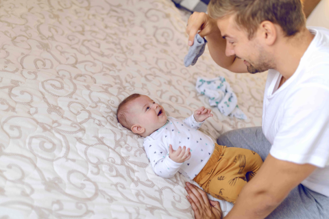 dad holding tiny baby socks and preparing to change clothes to his laughing child