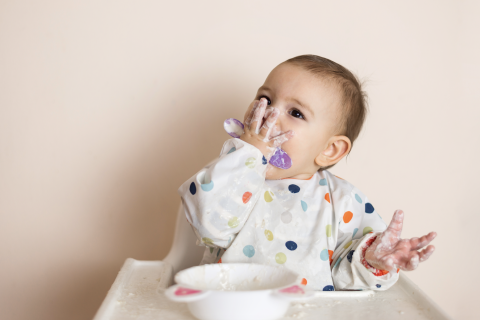 Baby eating mushy white food with a purple spoon