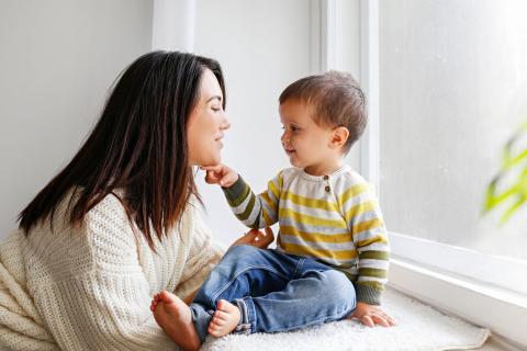 Mum and toddler look at eachother, toddler sat on windowsill