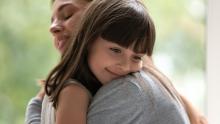 Smiling child puts her head on her mothers shoulder