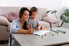 Mother and young boy sit on the floor at a table, drawing with coloured pencils and paper