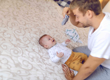 dad holding tiny baby socks and preparing to change clothes to his laughing child
