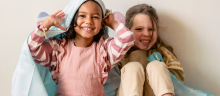 Two young girls playing under a blanket and smiling