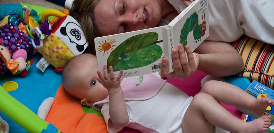 Mother lying on playmat with baby, reading the very hungry caterpillar book