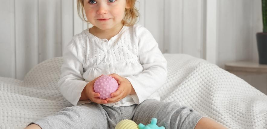 Young child playing with pastel coloured toys on a bed