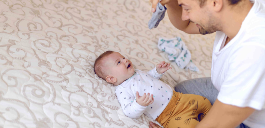 dad holding tiny baby socks and preparing to change clothes to his laughing child