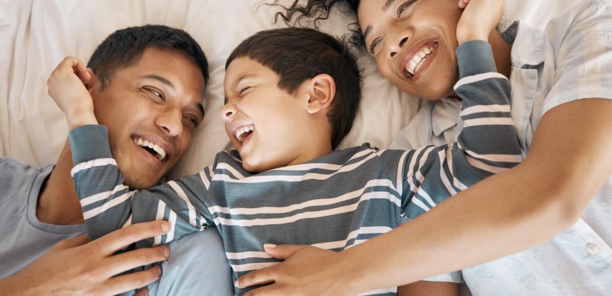 Family laughing and lying on a bed