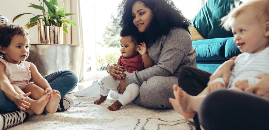 Mother and child sat on a rug with other toddlers and family members