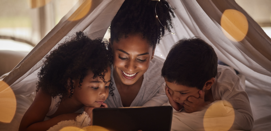 Mum and two children reading a book under a tent indoors