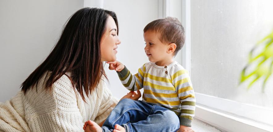 Mum and toddler look at eachother, toddler sat on windowsill