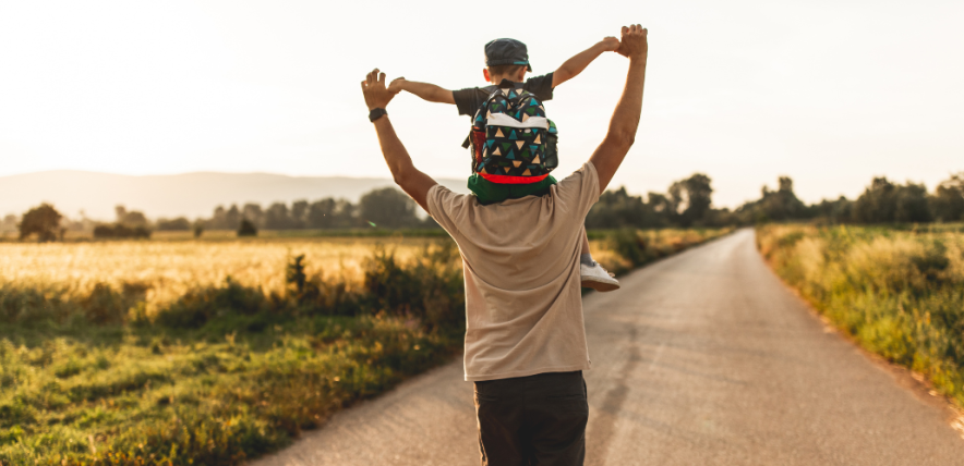 adult holding a child on his shoulders, walking down a rural path