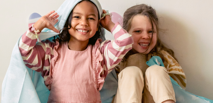 Two young girls playing under a blanket and smiling