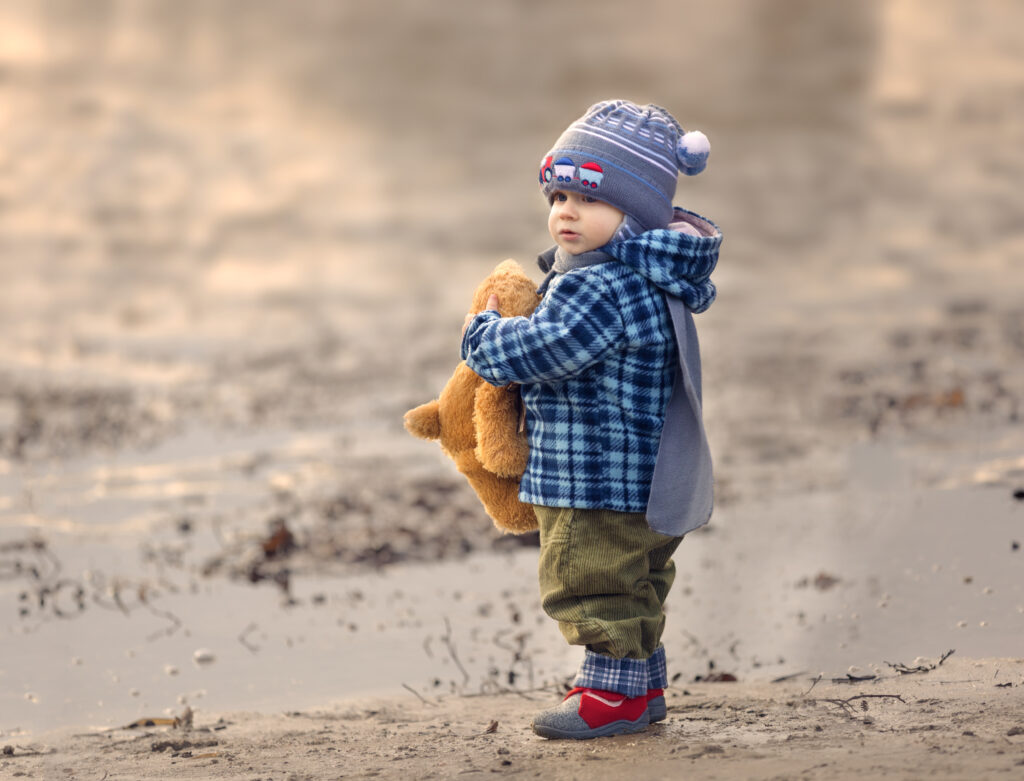 Child in a coat and hat holds a teddy bear and looks into the distance