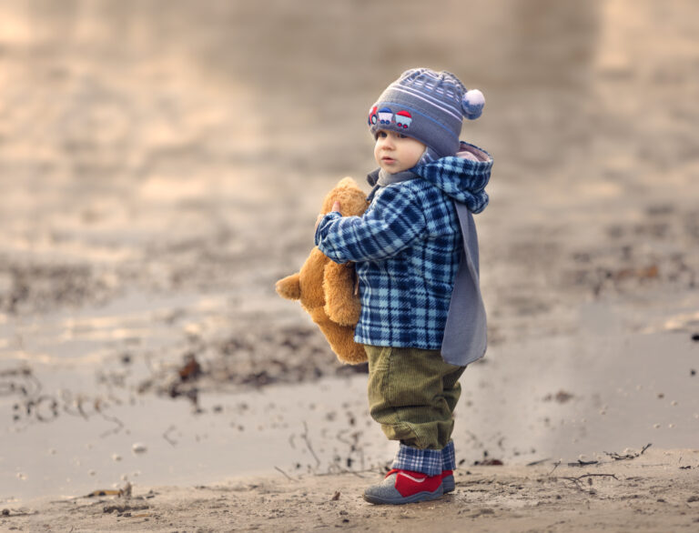 Child in a coat and hat holds a teddy bear and looks into the distance