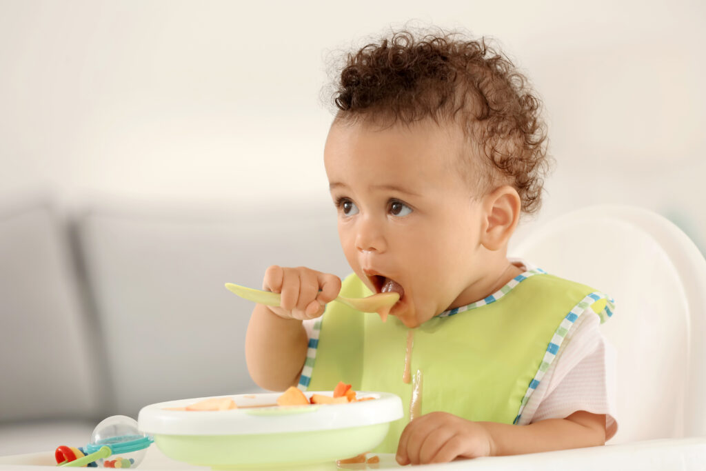 Young child eating pureed food in a high chair and green bib