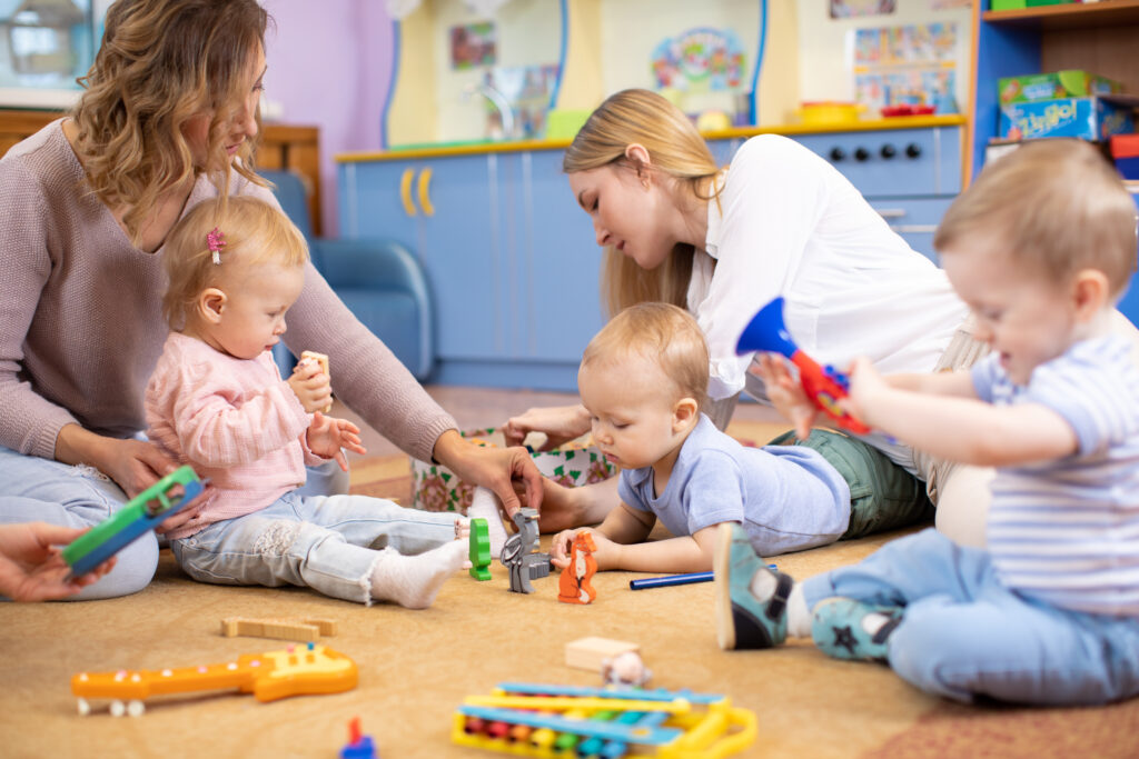 Group of mothers sat on the floor with their babies who are playing with colourful toys