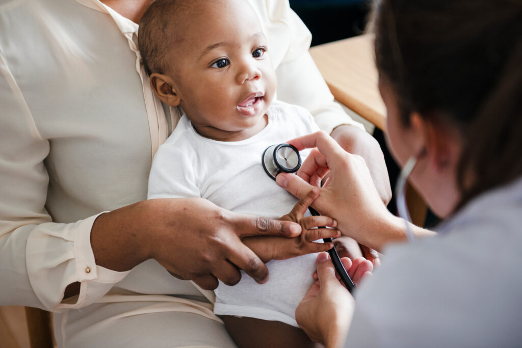 Baby being held on his mother's lap with a female doctor holding up a stethoscope to his chest