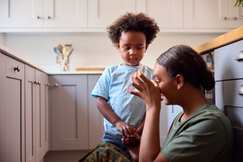 Woman sat on the kitchen floor wiping a tear from her face while her young son stands next to her looking concerned