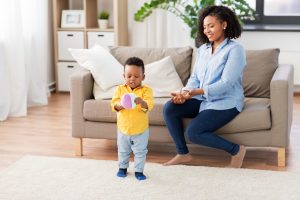 childhood, kids and people concept - happy african american mother and her baby son playing with ball together on sofa at home