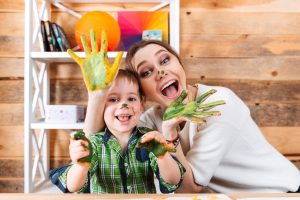 Cheerful excited mother and little son with painted hands in colorful paints having fun together